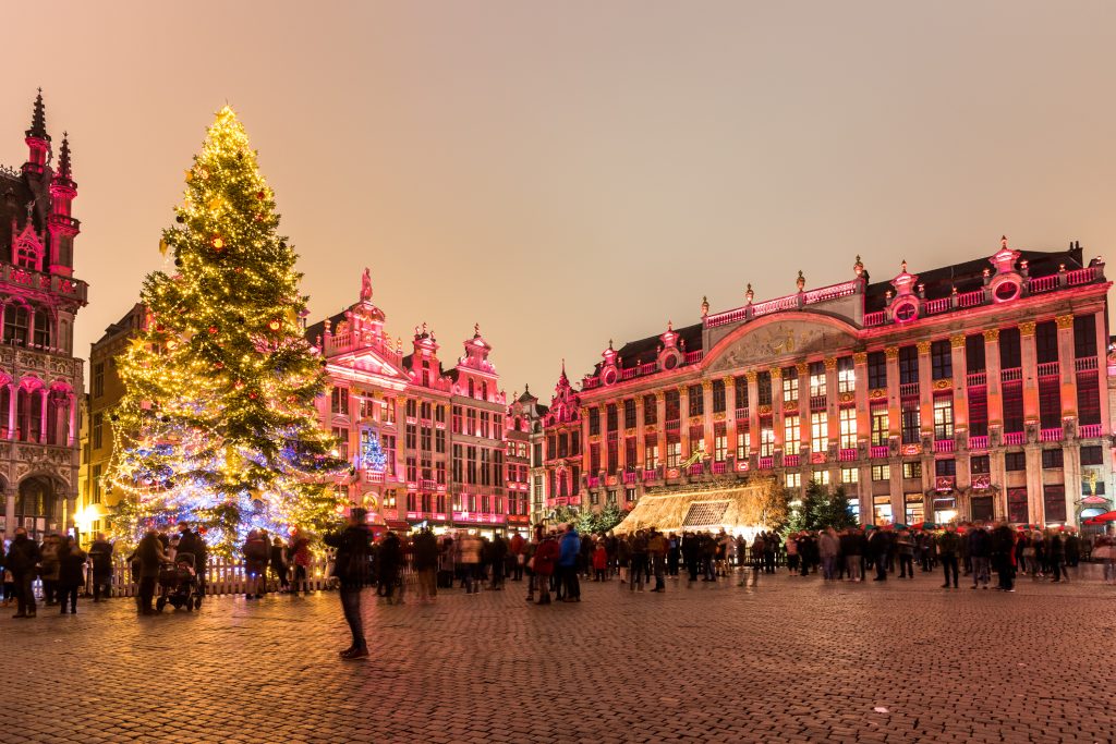 Christmas tree in a crowded square surrounded by illuminated historic buildings at night. Brussels, Belgium.